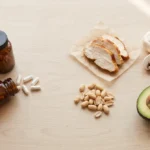 NMN vs niacinamide flat lay with unlabeled supplement bottles, capsules, chicken, peanuts, mushrooms and avocado